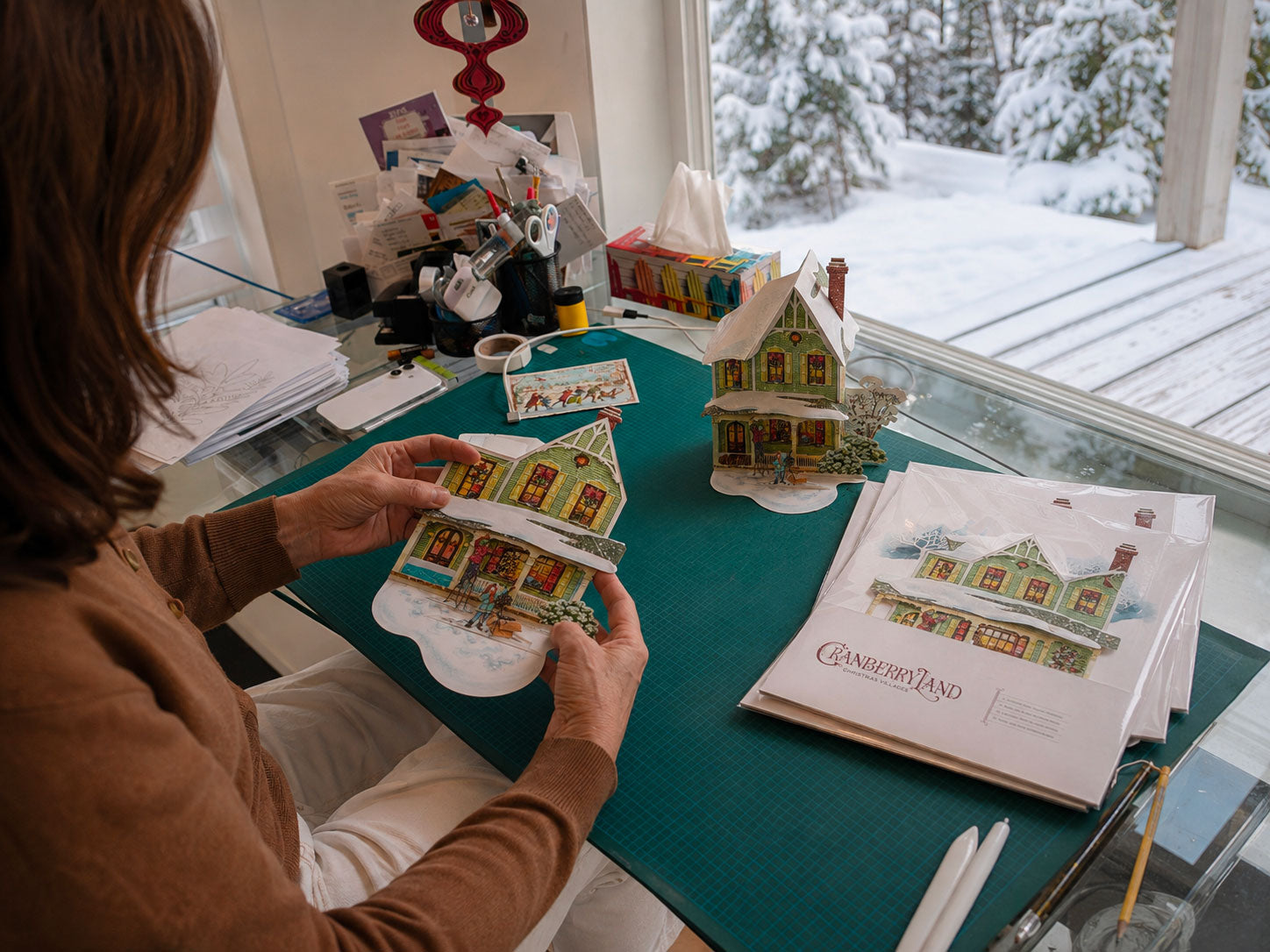 CranberryLand Christmas village house being folded flat by hand, with an assembled house and flat packaging nearby.